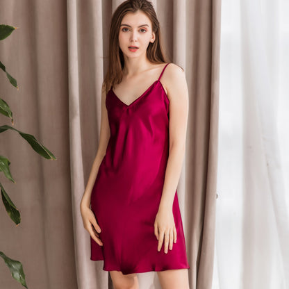 Woman wearing a red slip dress standing against a neutral curtain background